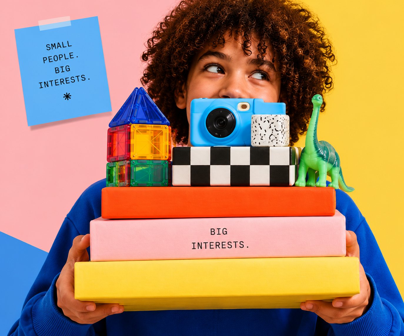 A child peers over a stack of colourful gift boxes topped with a toy camera, magnetic tiles and a toy dinosaur